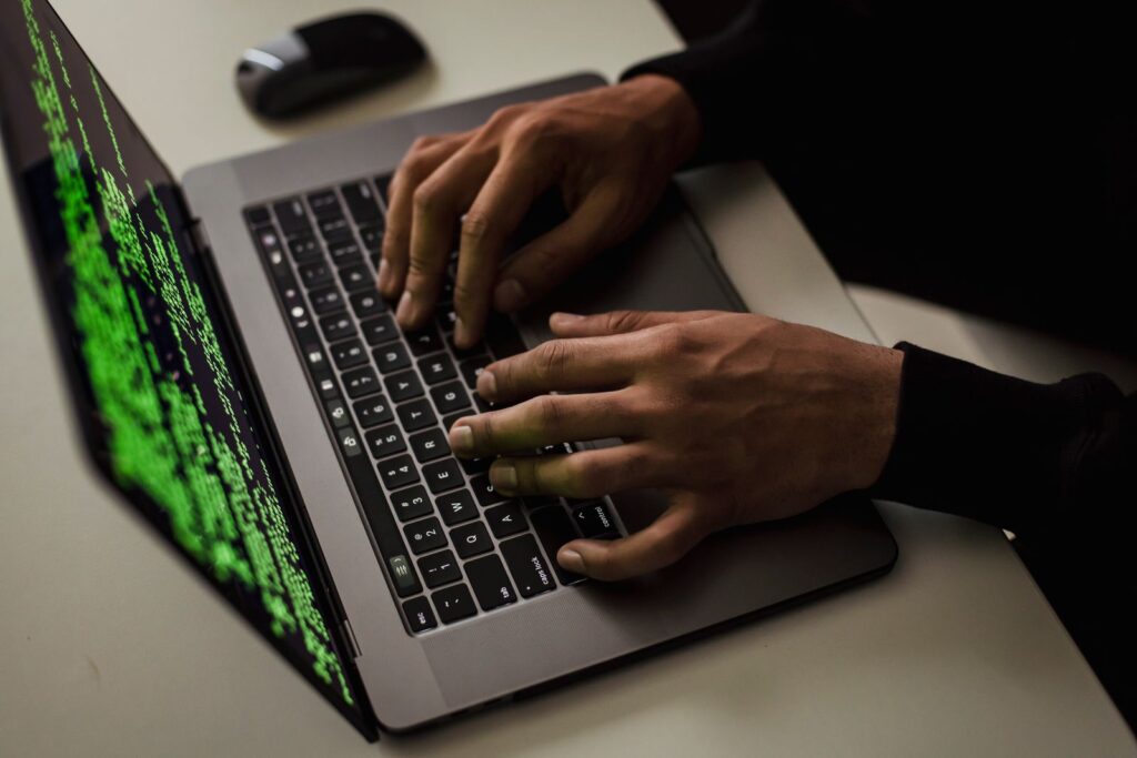 Person typing on a laptop with green code on the screen in a dark room
