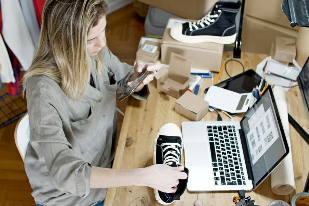 Small business owner using a phone and laptop to manage her shop listing
