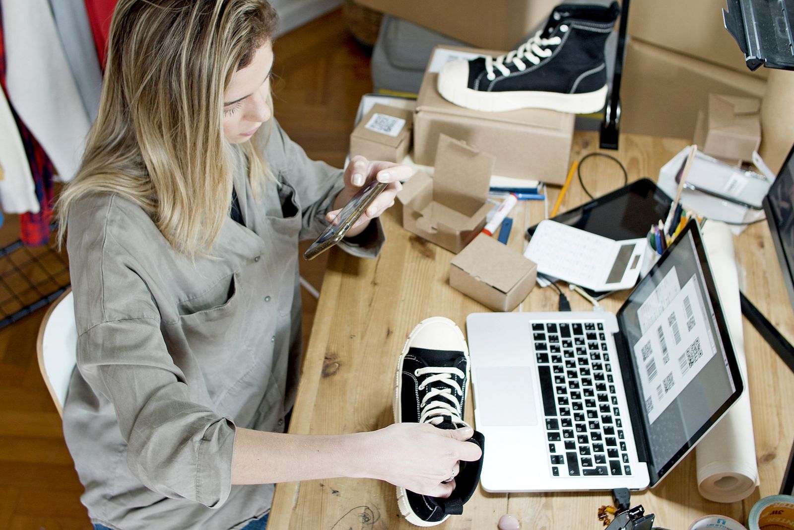 Small business owner using a phone and laptop to manage her shop listing