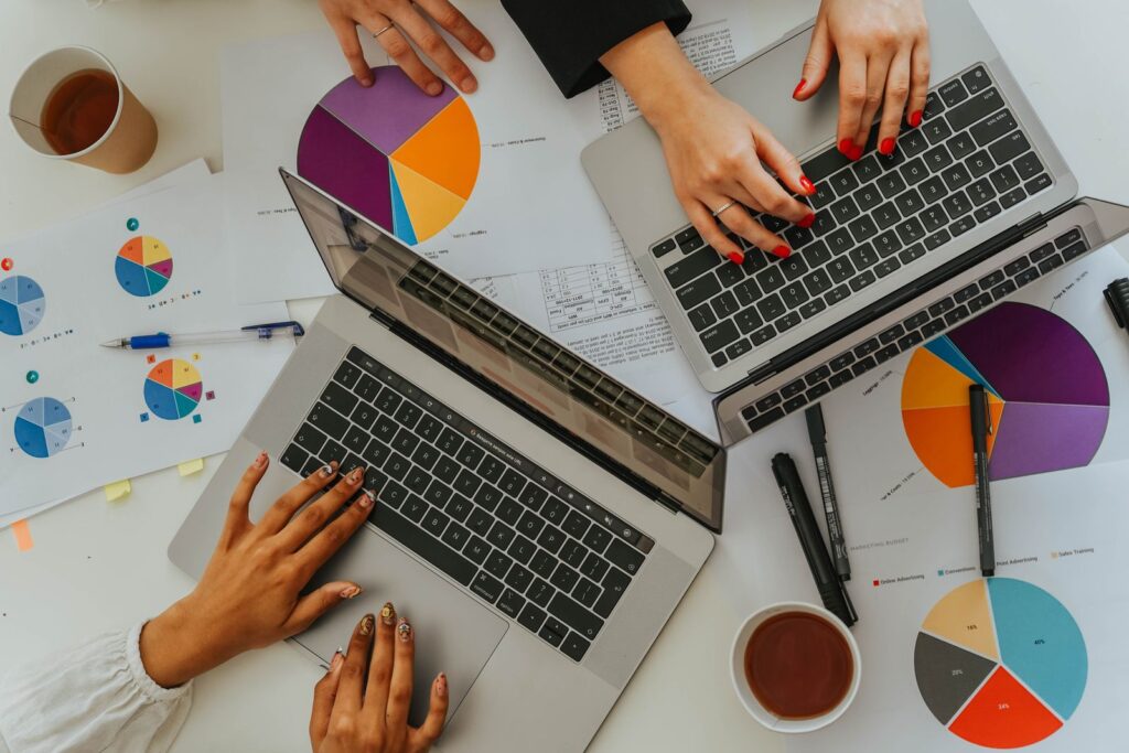 Two people reviewing budget charts and laptops on an office desk