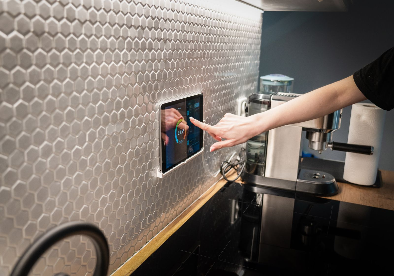 Homeowner using a wall mounted smart home control panel in a modern kitchen