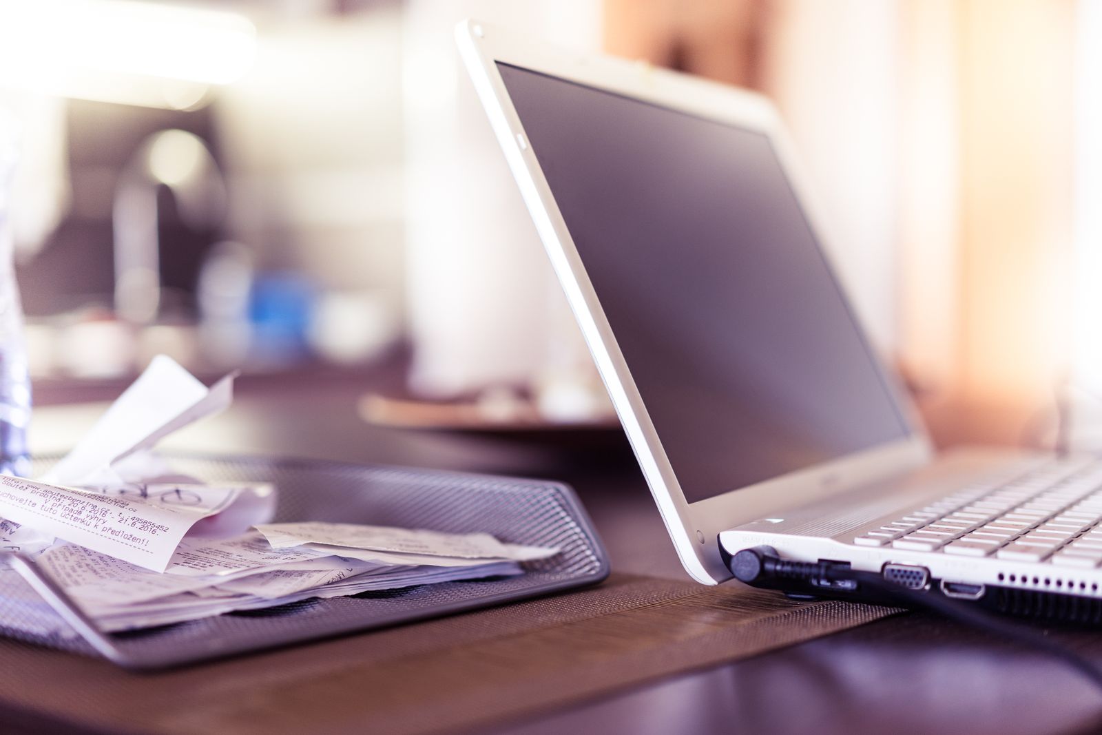 Paper invoices and receipts stacked beside an open laptop on an office desk