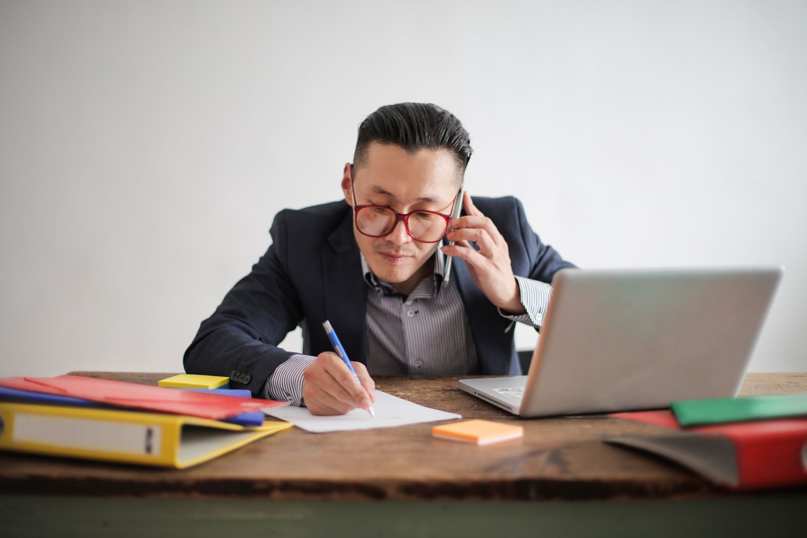 Business owner taking a phone call at an office desk while writing notes