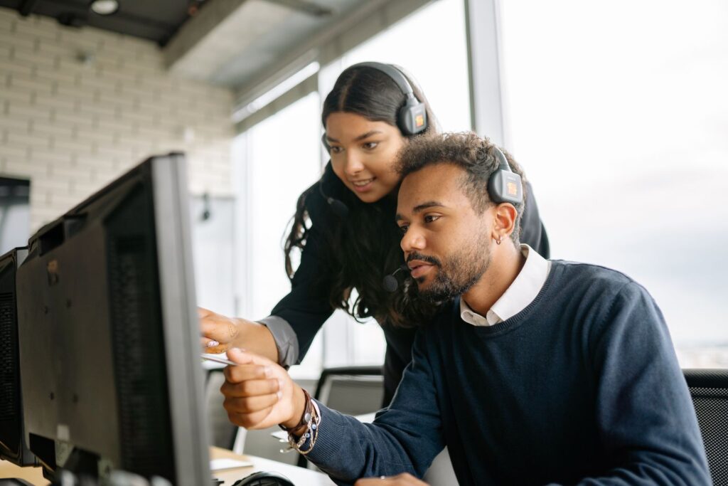Two IT help desk technicians with headsets reviewing an issue on a computer screen