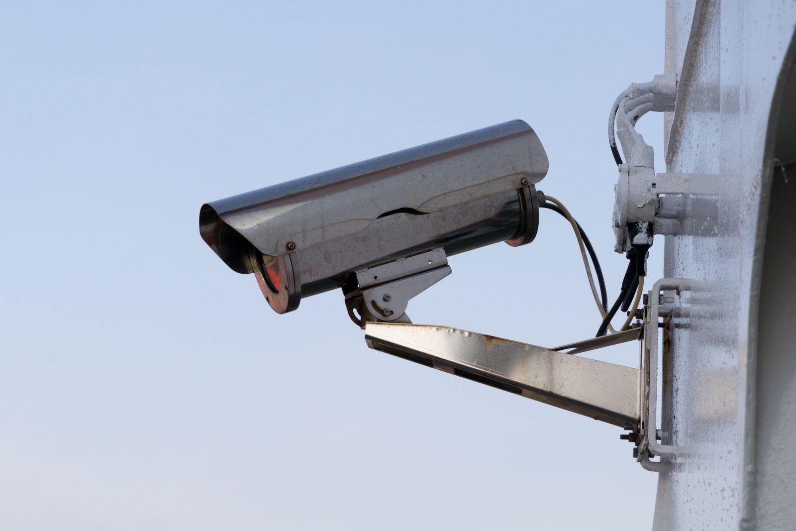 Outdoor home security camera mounted on an exterior wall against a clear sky