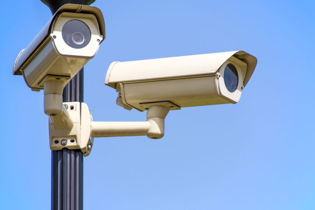 Two outdoor business security cameras mounted on a pole against a blue sky