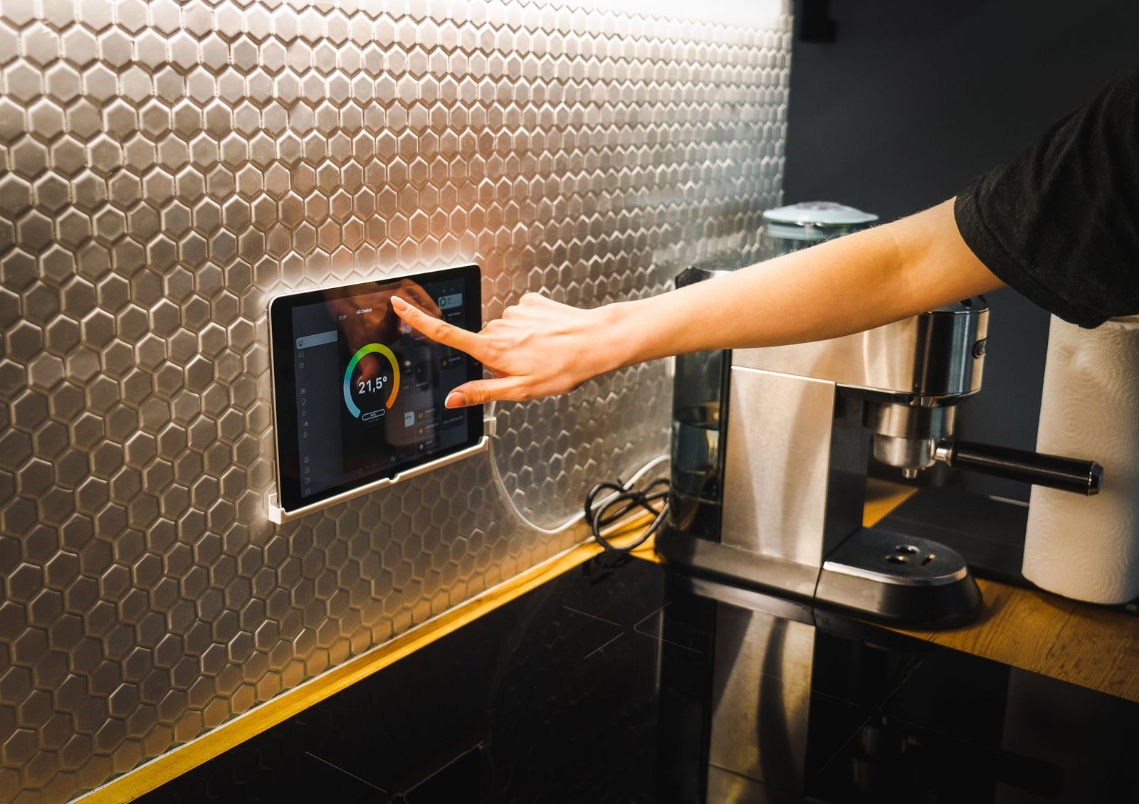 Homeowner tapping a wall mounted smart home control panel in a kitchen