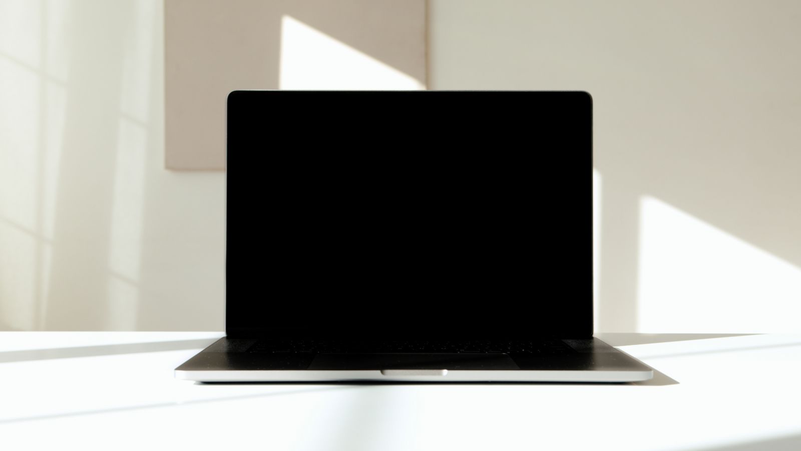 Laptop with a black screen that will not turn on, sitting on a white desk